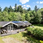 Holzhütte mit Solaranlage, Terrasse und Garten. Umgeben von Wald und Grün.