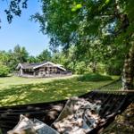 Hammock unter Bäumen mit Blick auf Holzhütte und Garten.