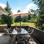 Terrasse mit Tisch, Stühlen und Sonnenschirm. Blick in einen grünen Wald.