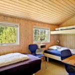 Zimmer mit Holzwand, zwei Betten und Tisch. Fenster zeigen Wald.