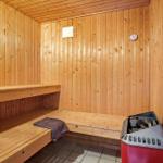 Sauna mit Holzwand und Sitzbänken, Heizung und Thermometer sichtbar.