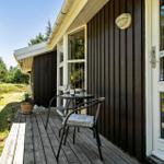 Terrasse mit Tisch, zwei Stühlen und Weinflasche vor einem Holzhaus mit Fenster und Tür.