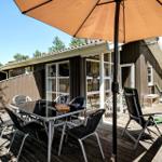 Terrasse mit Tisch, Stühlen und Sonnenschirm vor einem Haus mit Holzfassade.