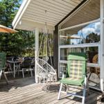 Terrasse mit grünen Stühlen, Sonnenschirm und Hängesessel. Durchgehende Glasfront zum Innenraum.