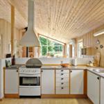 Küche mit weißen Schränken, Steinplatten und Holzverkleidung. Blick in Schlafzimmer.