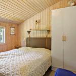 Schlafzimmer mit Holzwand, Bett, Kleiderschrank und Fenster mit Blick auf Wald.