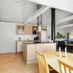 Küche mit Essbereich und Wohnzimmer im Hintergrund. Holzfußboden und weiße Decken.
