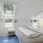 Schlafzimmer mit Doppelbett, Dachfenster und gelbem Wandpaneel.