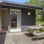 Terrasse mit Picknicktisch vor einem dunklen Holzhaus. Durch Fenster und Tür ist Innenraum sichtbar.