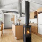 Küche mit Holzschrank, Kaminofen und Esstisch. Weiße Wände und Holzboden.