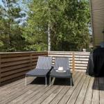 Terrasse mit zwei Liegestühlen und Holzgeländer. Hintergrund: Bäume und Hauswand.