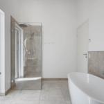 Bad mit Dusche und freistehender Badewanne, großes Fenster mit Blick auf Grünfläche.
