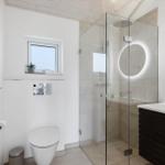 Moderne Badewanne mit Dusche, Waschbecken und Toilette. Ein Fenster mit Pflanze.