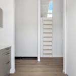 Küche mit grauen Schränken und Holzboden. Treppe führt zu einem Dachboden.