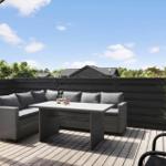 Terrasse mit Sitzgruppe, Tisch und Pflanze. Hintergrund: Holzzaun und Häuser.