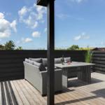 Terrasse mit Sitzgruppe, Tisch und Flasche. Holzdecke, schwarze Umzäunung, Himmel mit Wolken.