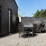 Terrasse mit Tisch, Stühlen und Grill, angrenzend an ein schwarz verkleidetes Haus.