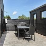 Terrasse mit Tisch, Stühlen und Grill. Holzwand und Dachrinnen sichtbar.