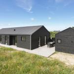 Moderne schwarze Holzhütte mit Terrasse und Garten. Außentisch und Sitzgelegenheiten.
