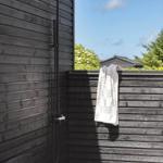 Außen-Dusche mit Duschbrause an schwarzer Holzwand. Handtuch hängt an der Wand.