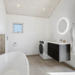Badezimmer mit freistehender Badewanne, Waschmaschine und beleuchtetem Spiegel.