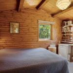 Schlafzimmer mit Holzwand, Bett, Schreibtisch und Fenstern.