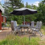 Holzterrasse mit Tisch, Stühlen und Sonnenschirm neben rotem Haus.