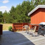 Terrasse mit Tisch, Stühlen und Grill neben rotem Holzhaus. Hintergrund: Wald.