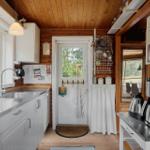 Küche mit Holzwand, Fenster, Spüle und Kochfeld. Tür führt nach draußen.