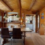 Esszimmer mit Holzdecke, Tisch und Stühle. Küche und Wohnbereich sichtbar.