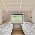 Zwei Betten in einem holzverkleideten Raum mit Fenster und Heizung.
