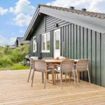 Holzterrasse mit Tisch und Stühlen vor einem grauen Holzhaus mit Dach und Fenstern.