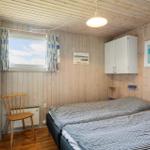 Schlafzimmer mit Holzwand, Bett, Stuhl und Fenster mit Vorhängen.