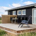 Holzterrasse mit Tisch, Stühlen und Liegestuhl vor einem schwarz getünchten Haus.