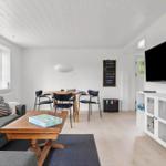 Wohn- und Essbereich mit Sofa, Tisch, Stühlen und Fernseher an der Wand.