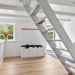 Raum mit Holzboden, weißer Treppe und Fenster mit Blick auf Grün.
