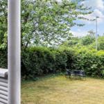 Garten mit Tisch und Stühlen, umgeben von Bäumen und Sträuchern unter blauem Himmel.