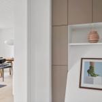 Ein Raum mit Holztisch, Stühlen und einer weißen Decke. An der Wand hängt ein Bild und ein Vase auf einer Ablage.