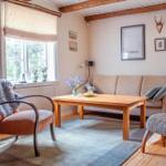 Wohnzimmer mit Sofa, Tisch und Stühlen. Holzbalken an der Decke und Fenster mit Blick nach draußen.