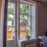 Durch das Fenster blickt man auf eine Holzterrasse und ein rotes Gebäude.
