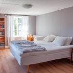 Schlafzimmer mit Bett, Bücherregal und Fenster. Holzboden und weiße Wände.
