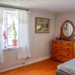 Schlafzimmer mit Holzboden, Bett, Schrank und Fenster mit Vorhängen.