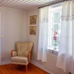 Ein Raum mit einem Sessel, einem Fenster mit weißen Vorhängen und zwei Bildern an der Wand.