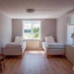 Zwei Betten, Fenster mit Blick, Holzboden, Stuhl und Lampe.