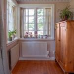 Raum mit Holzboden, Fenster, Pflanzen und Holzschrank.