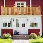 Rotes Holzhaus mit weißer Eingangstür, Balkon und Blumenbeeten.