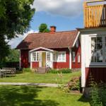 Rotes Haus mit Terrasse, Garten und Tisch. Helle Fenster, roter Dachfirst.