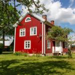 Rotes Holzhaus mit weißen Fensterrahmen und Garten. Hinterhof mit Holzterrasse und Bäumen.