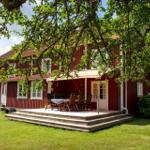 Rotes Holzhaus mit Terrasse und Garten. Tisch und Stühle auf der Veranda.