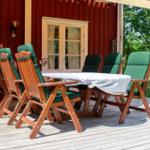 Terrasse mit Holztisch und grünen Stühlen vor rotem Holzhaus.